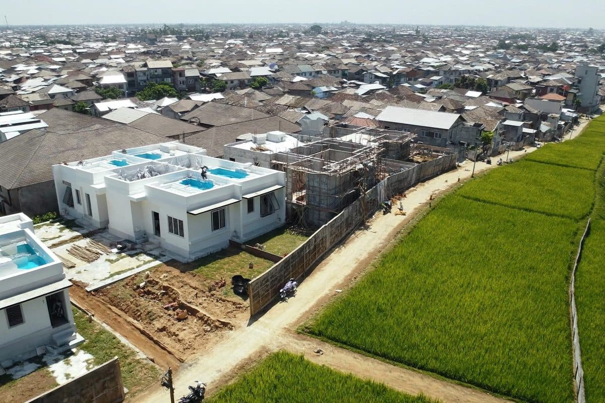 Aerial view of newly built villas with pools packed against the last strip of rice paddy in Bali