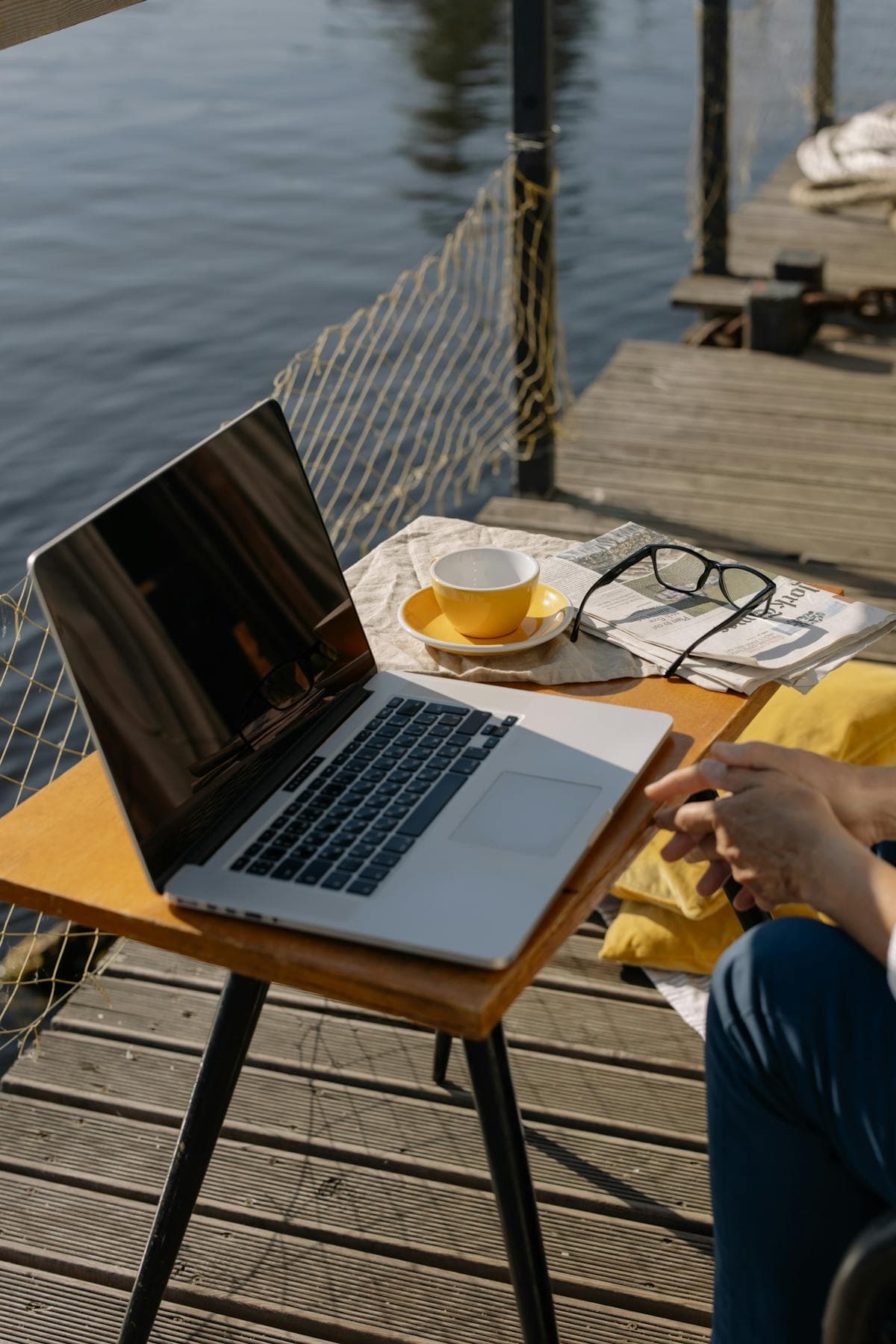Laptop, coffee cup and glasses on a small table on a wooden jetty above the water