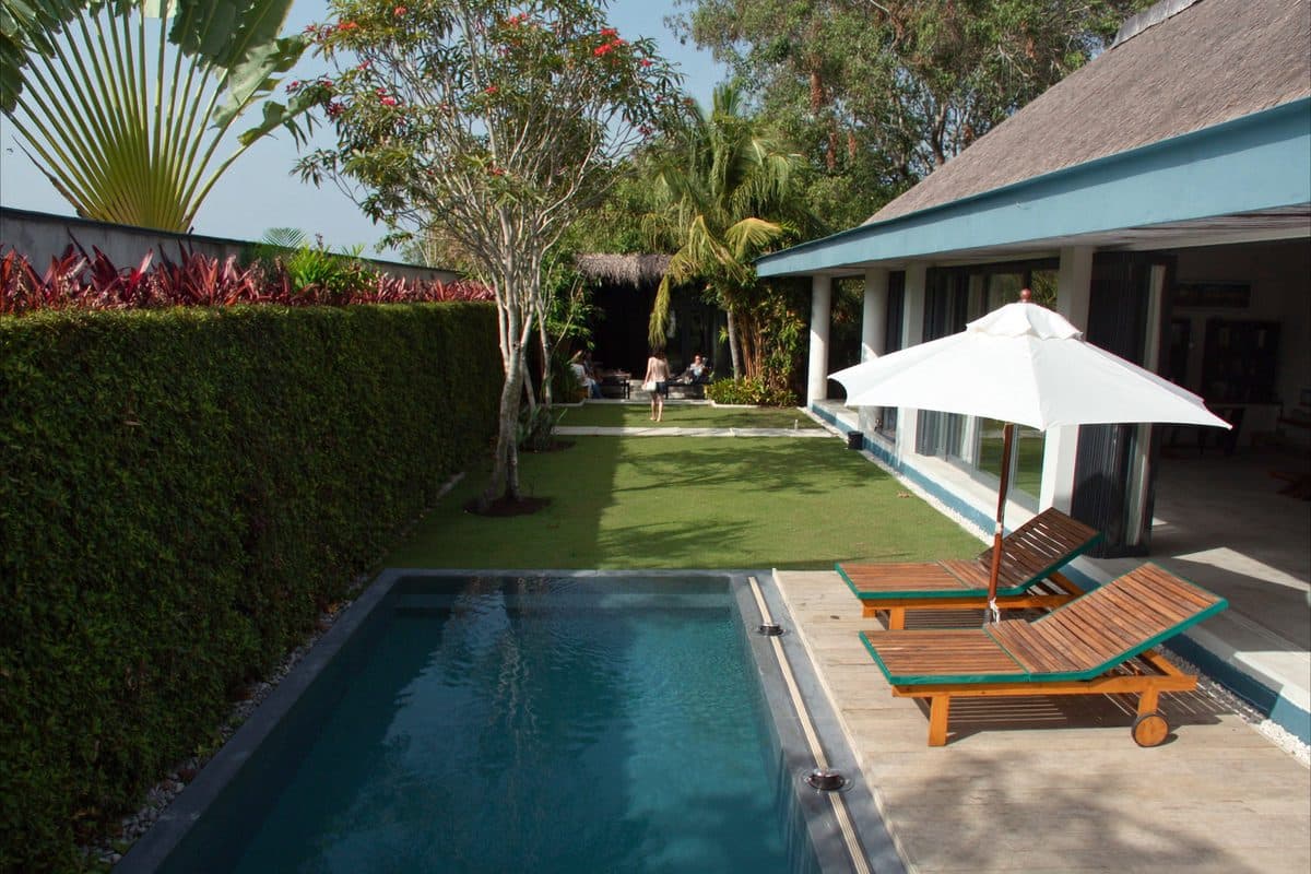 Narrow lap pool and sun loungers under a white parasol beside a single-storey villa