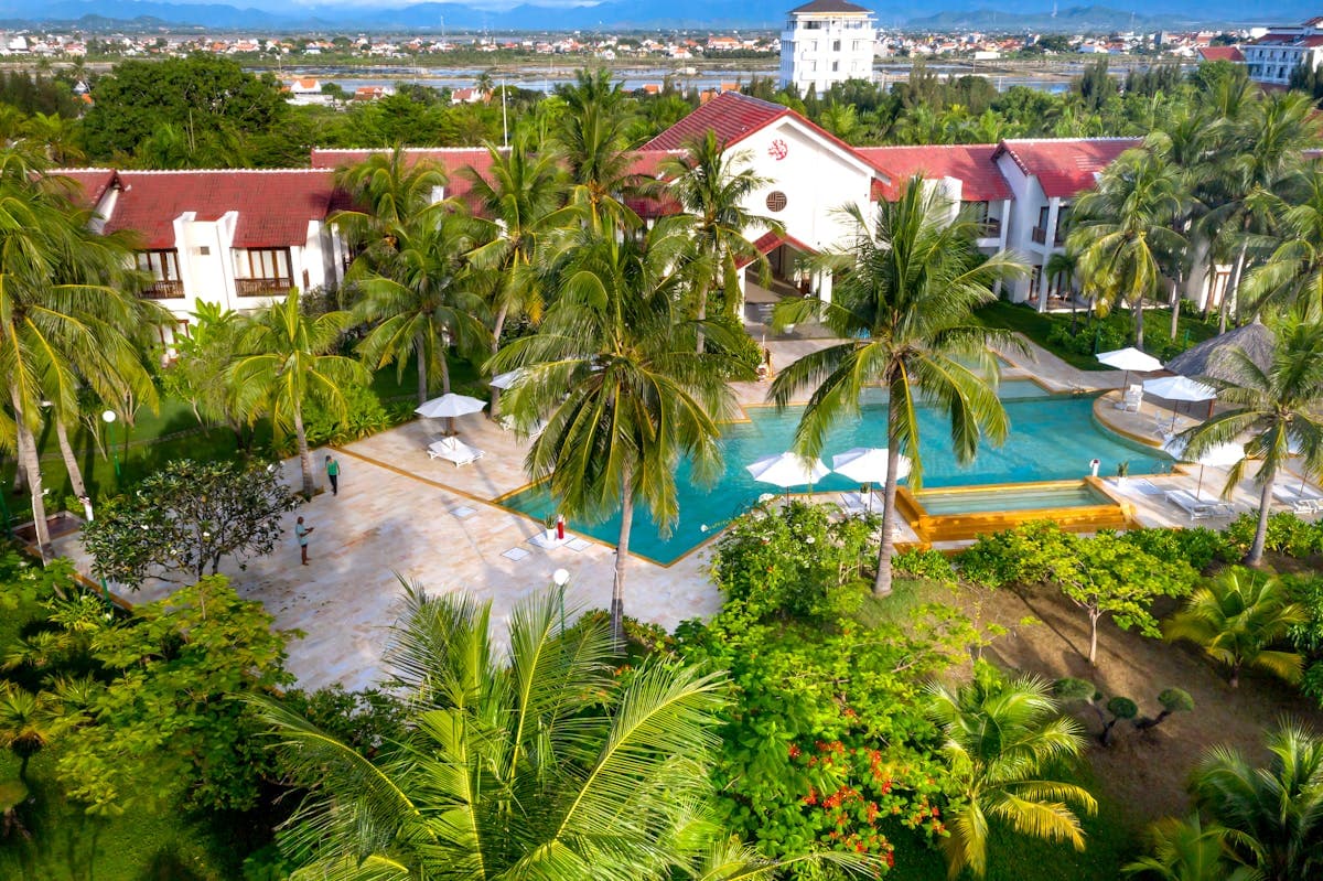 Aerial view of a palm-fringed swimming pool among red-tiled villa roofs