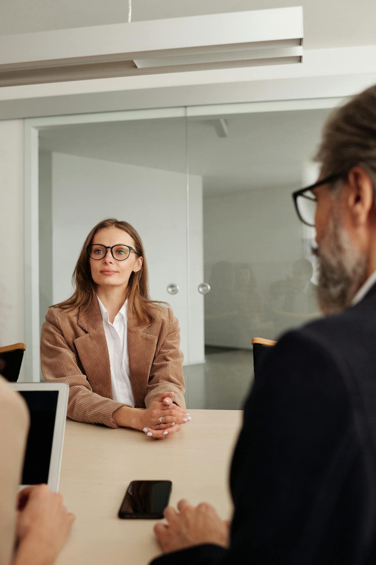 Woman in a blazer sitting across a meeting table from a man in a glass-walled office