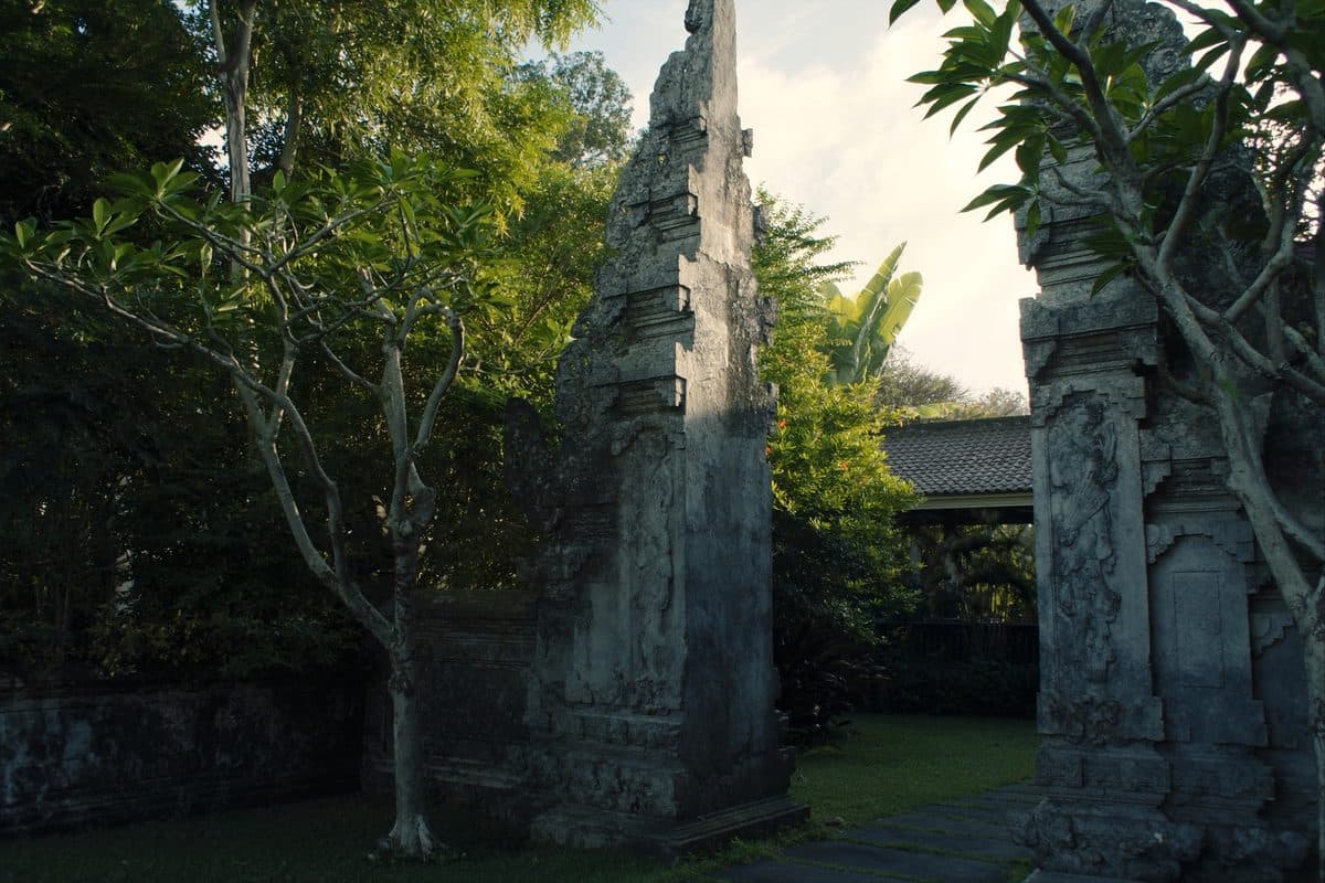 Carved split candi bentar stone gateway to a Balinese villa compound, framed by frangipani trees