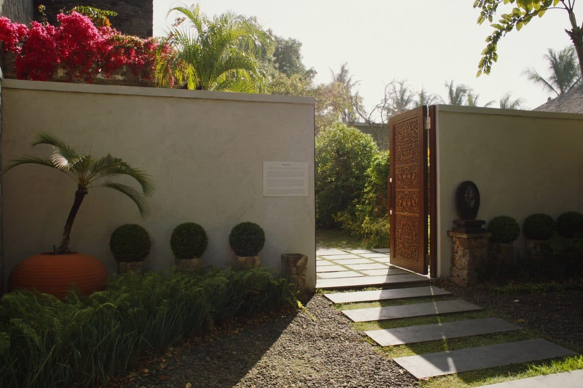 Carved wooden gate standing open in a garden wall, with stepping stones leading through